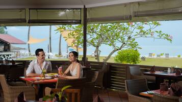 A restaurant with wicker furniture, outdoor seating, and a view of the beach.