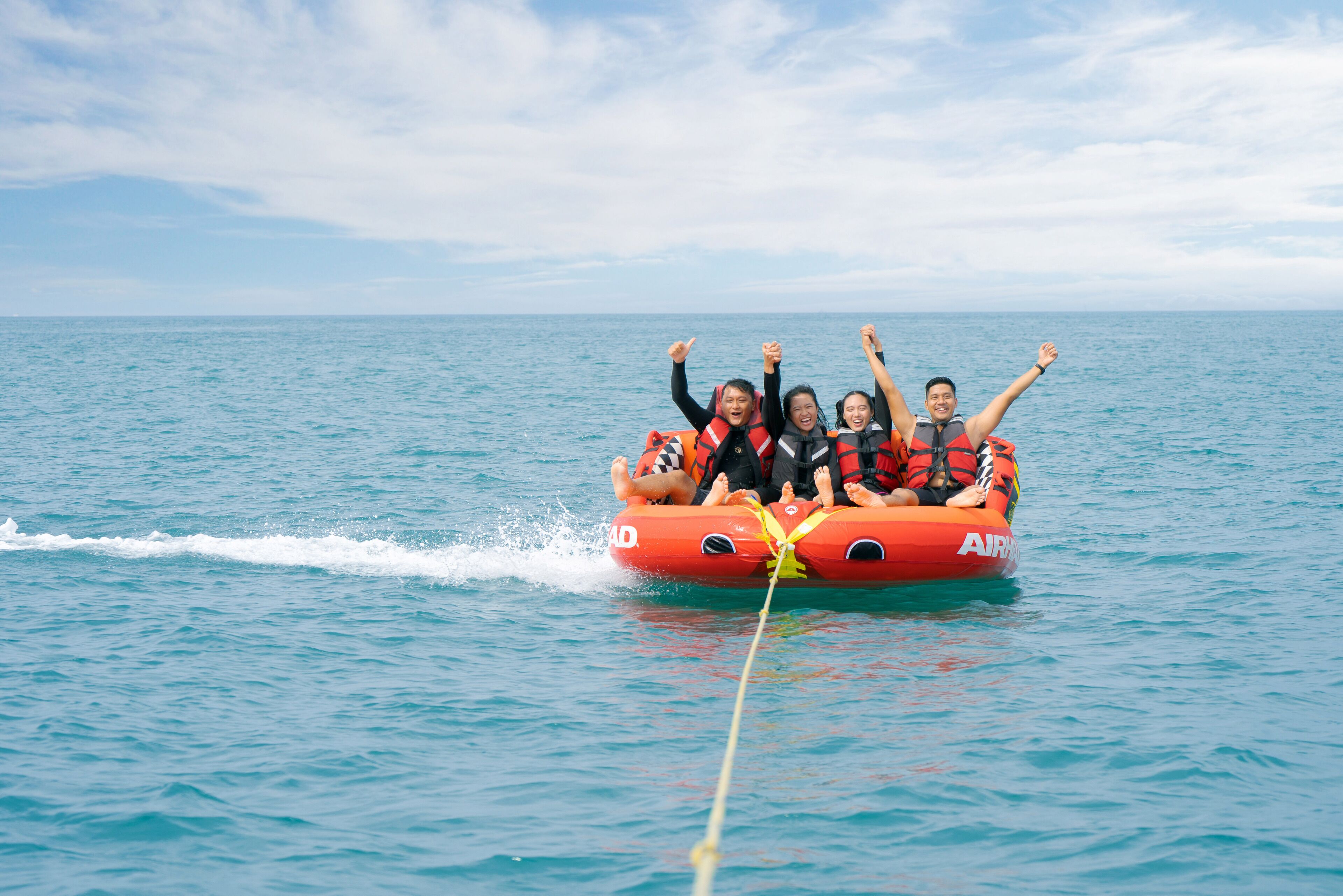 A group of people on a red inflatable raft with a wake behind it, floating on calm blue water.