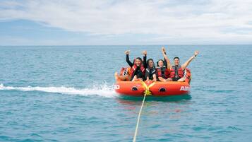 A group of people on a red inflatable raft with a wake behind it, floating on calm blue water.