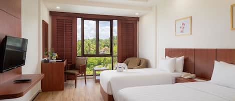 A hotel room with two beds, a desk with a flat-screen TV, a chair, a small table, and a ceiling fan.