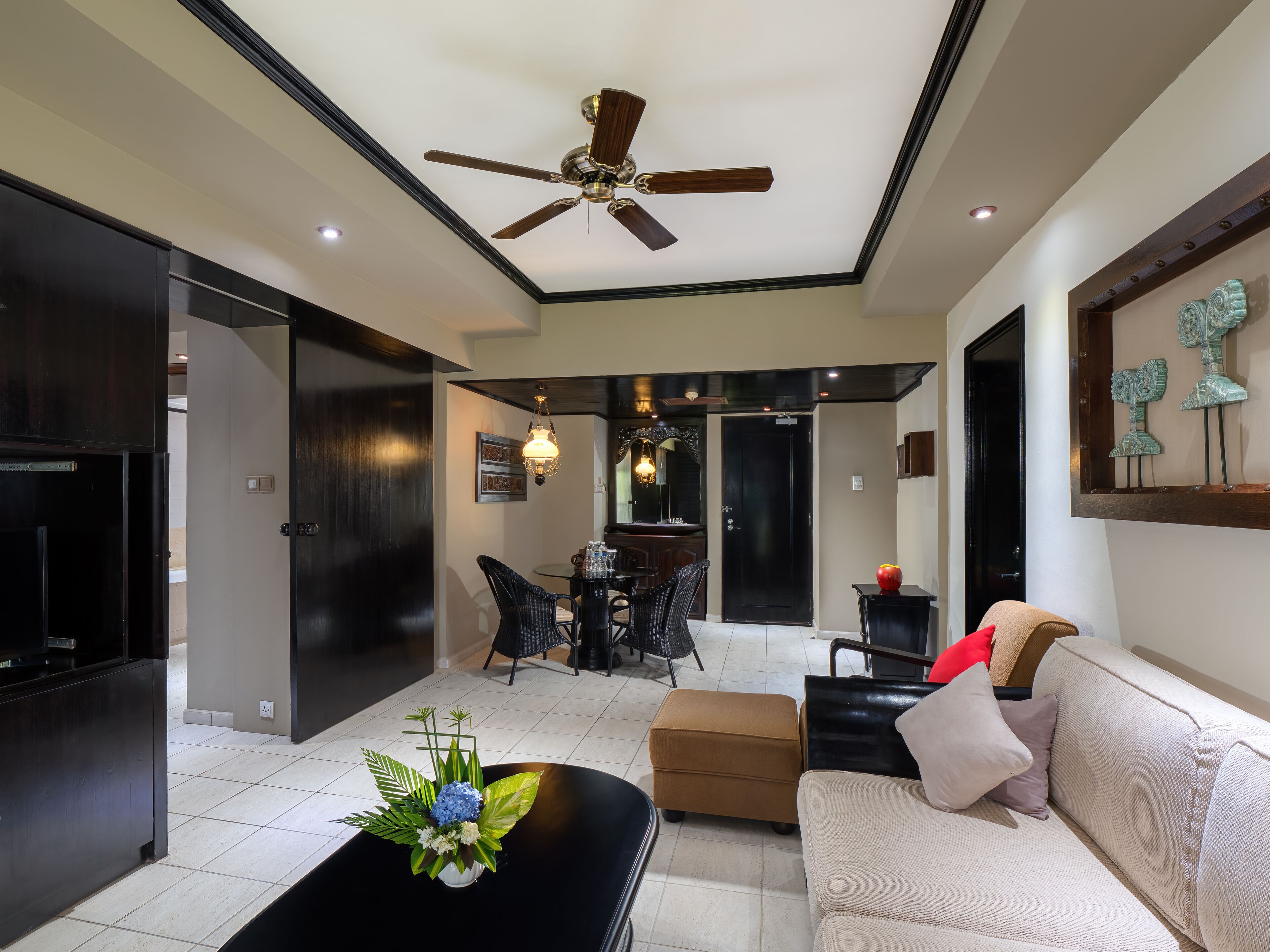 A modern living room with a ceiling fan, a coffee table with a floral arrangement, a sofa, and a dining area with a chandelier.