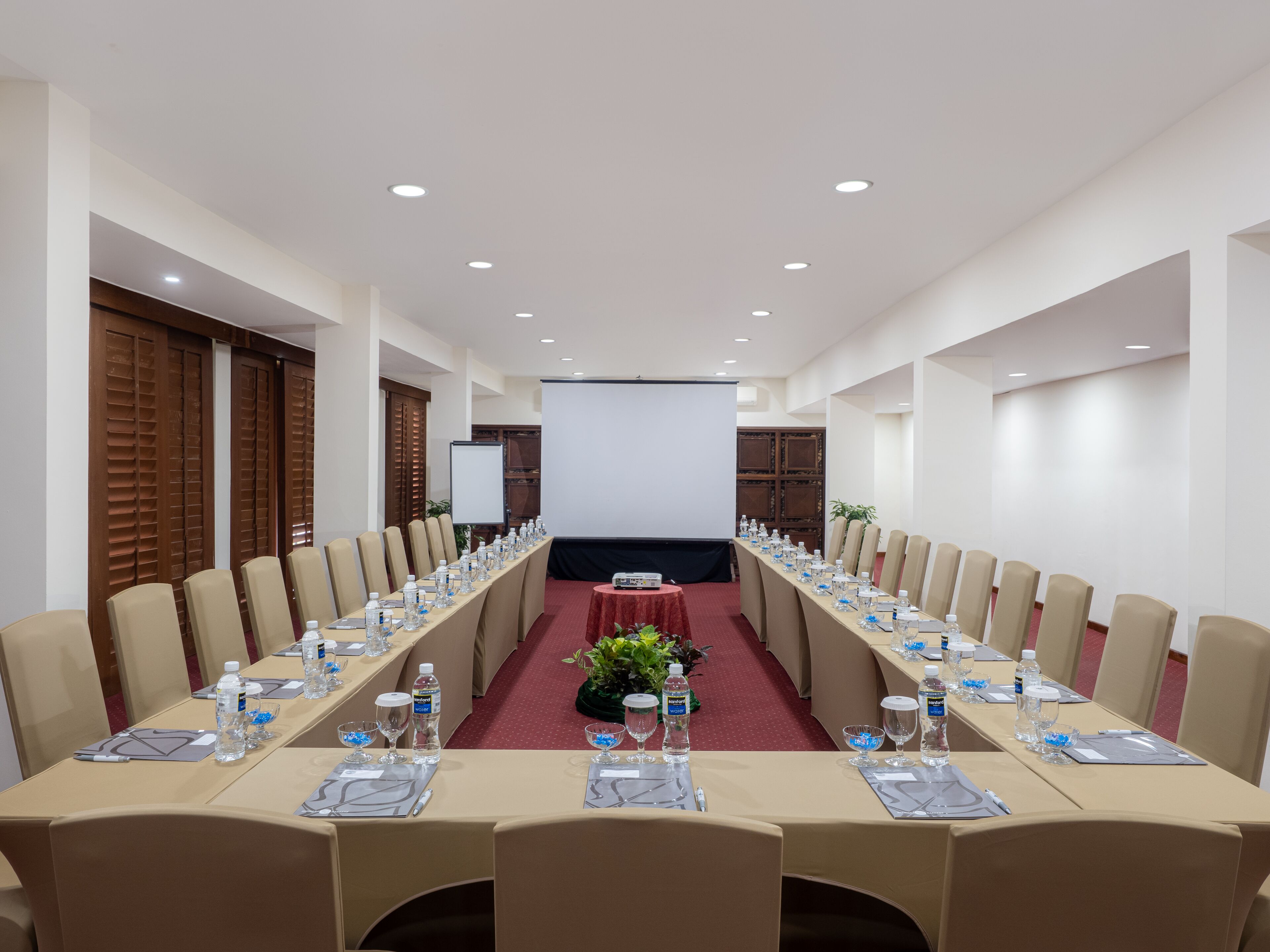 A conference room with a long table, chairs, water bottles, and a projector screen.