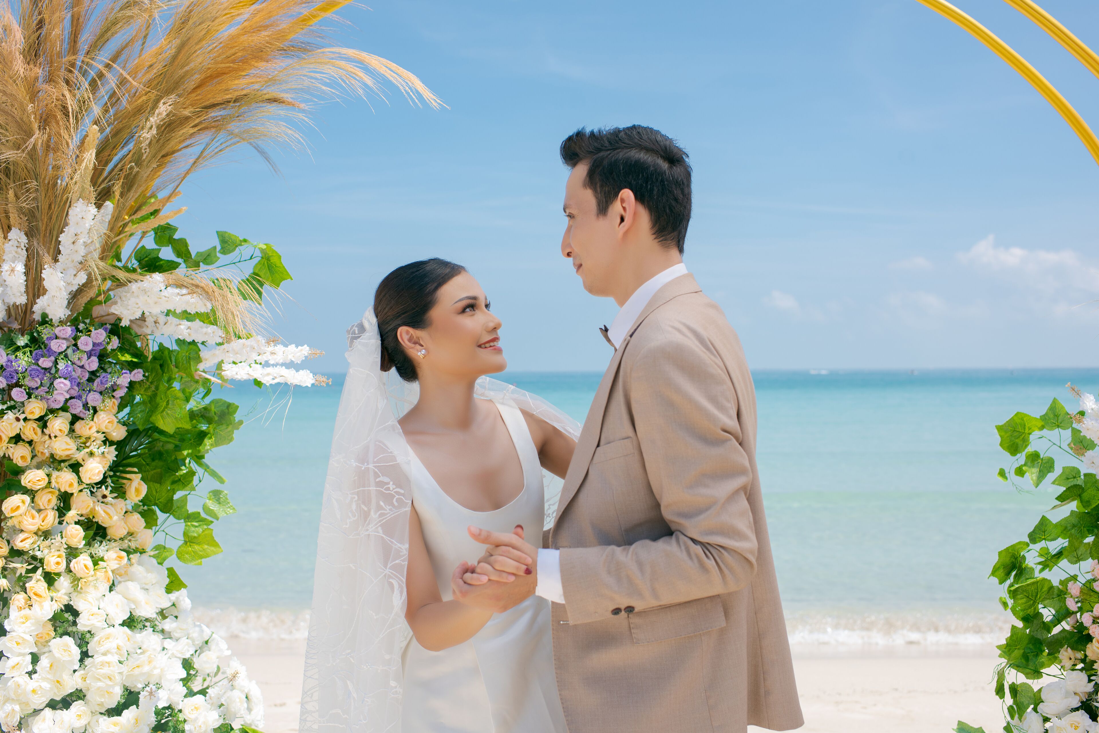 Un couple se tient devant une arche décorée de fleurs sur une plage.