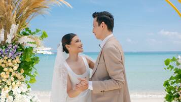 Un couple se tient devant une arche décorée de fleurs sur une plage.