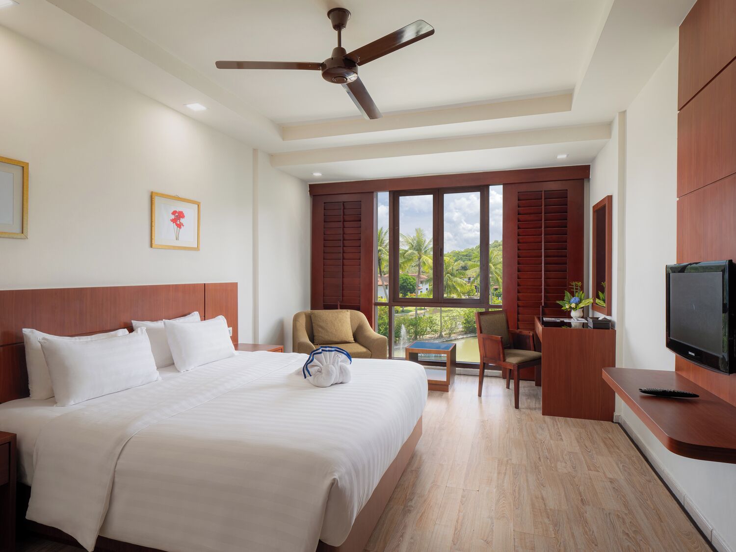 A hotel room with a bed, a desk, a chair, a television, and a window with a view of palm trees.