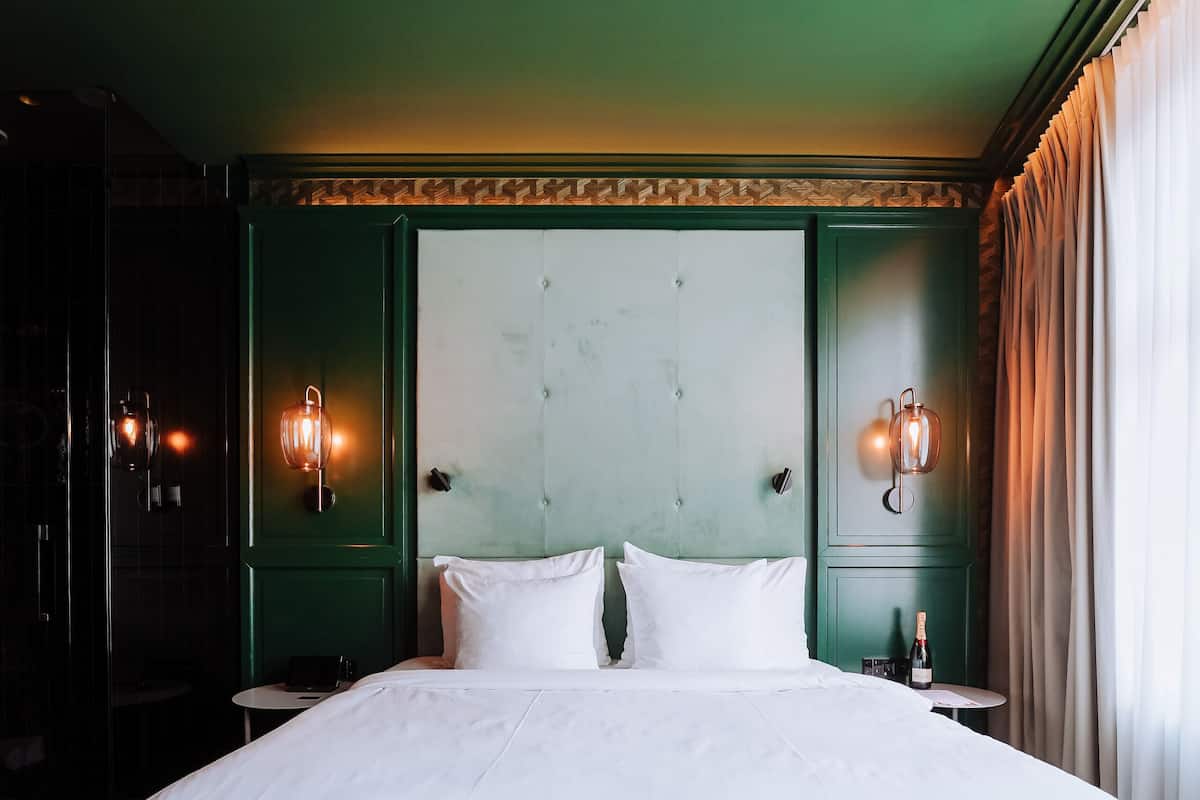 Un grande letto con lenzuola bianche, una testiera imbottita verde e due applique a parete.