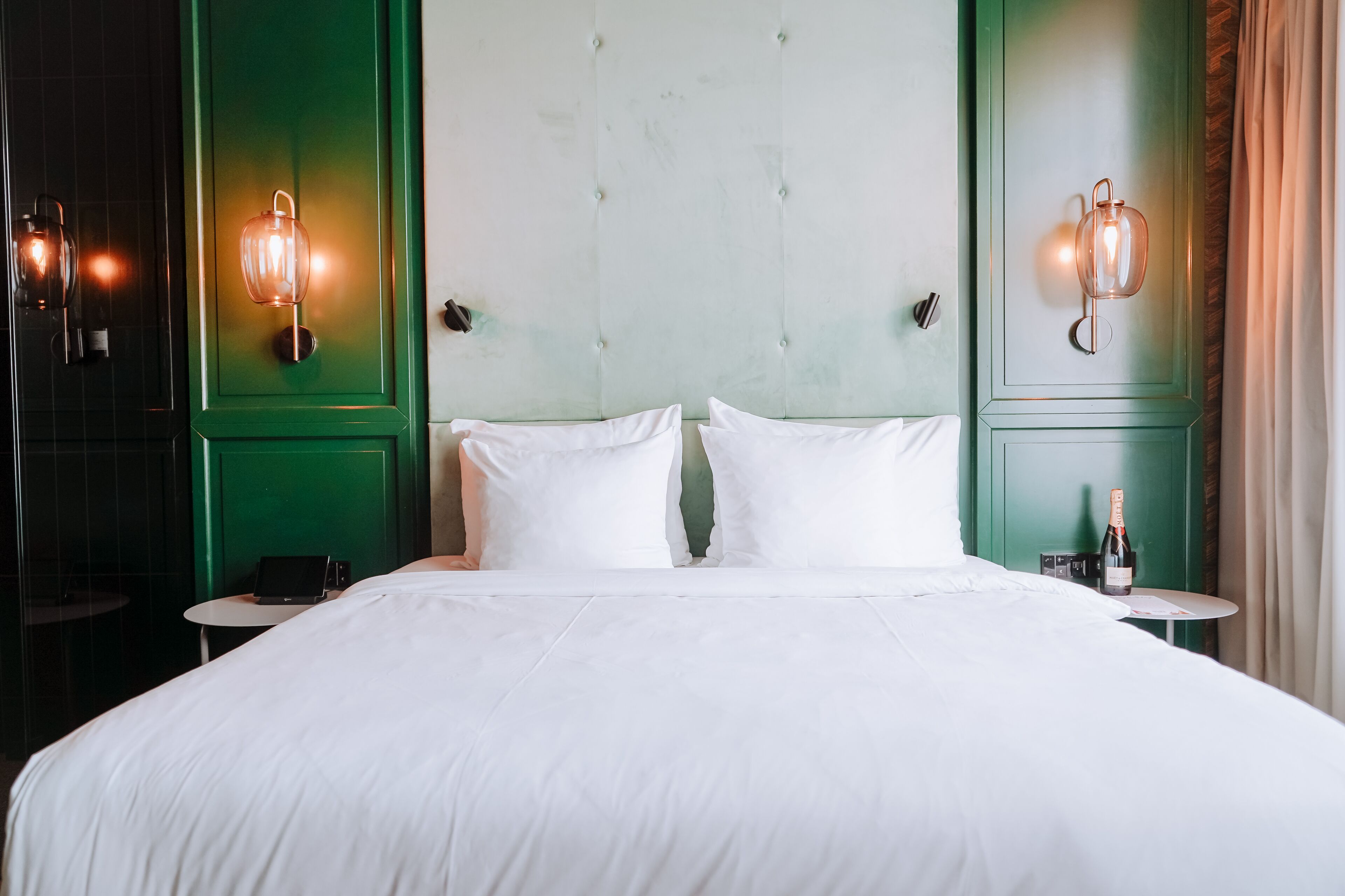 A neatly made bed with white linens, two bedside tables, and wall-mounted sconces.