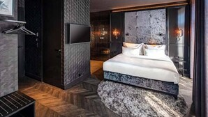A modern bedroom with a large bed, a TV mounted on the wall, and a unique textured wall design. - The Highlander (Amsterdam)