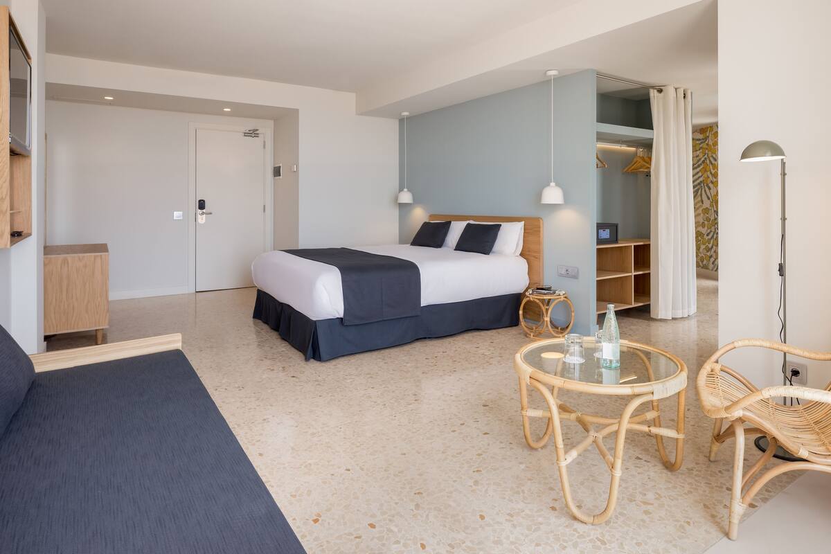 Ein modernes Hotelzimmer mit einem Bett, einem kleinen runden Tisch mit Stühlen, einem Kleiderschrank und einem Spiegel.