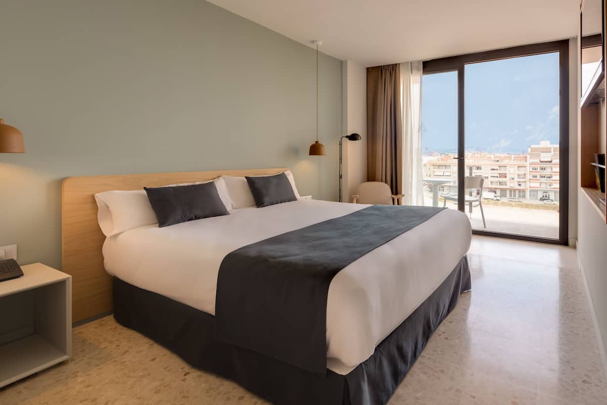 Ein modernes Hotelzimmer mit einem großen Bett, einem Schreibtisch und Blick auf die Stadt durch große Fenster.