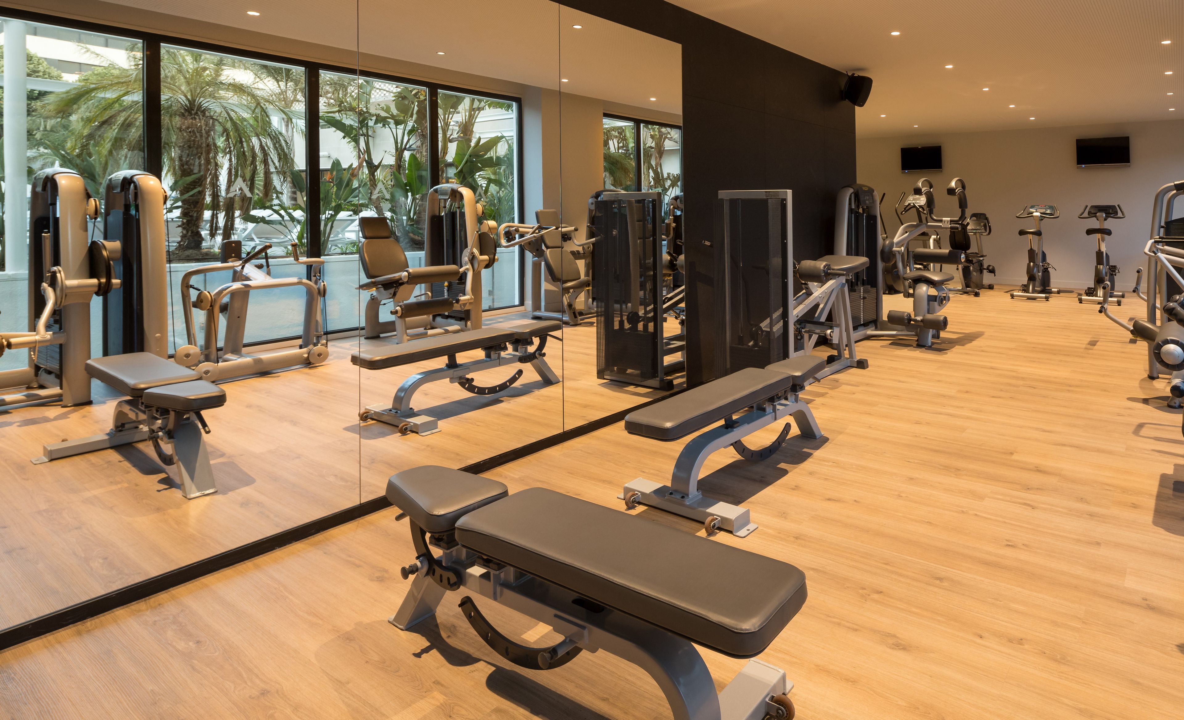 A gym with various exercise equipment, large windows, and a wooden floor.