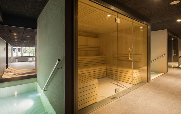 Una sauna moderna con paredes de vidrio, un banco de madera y un pasamanos metálico.