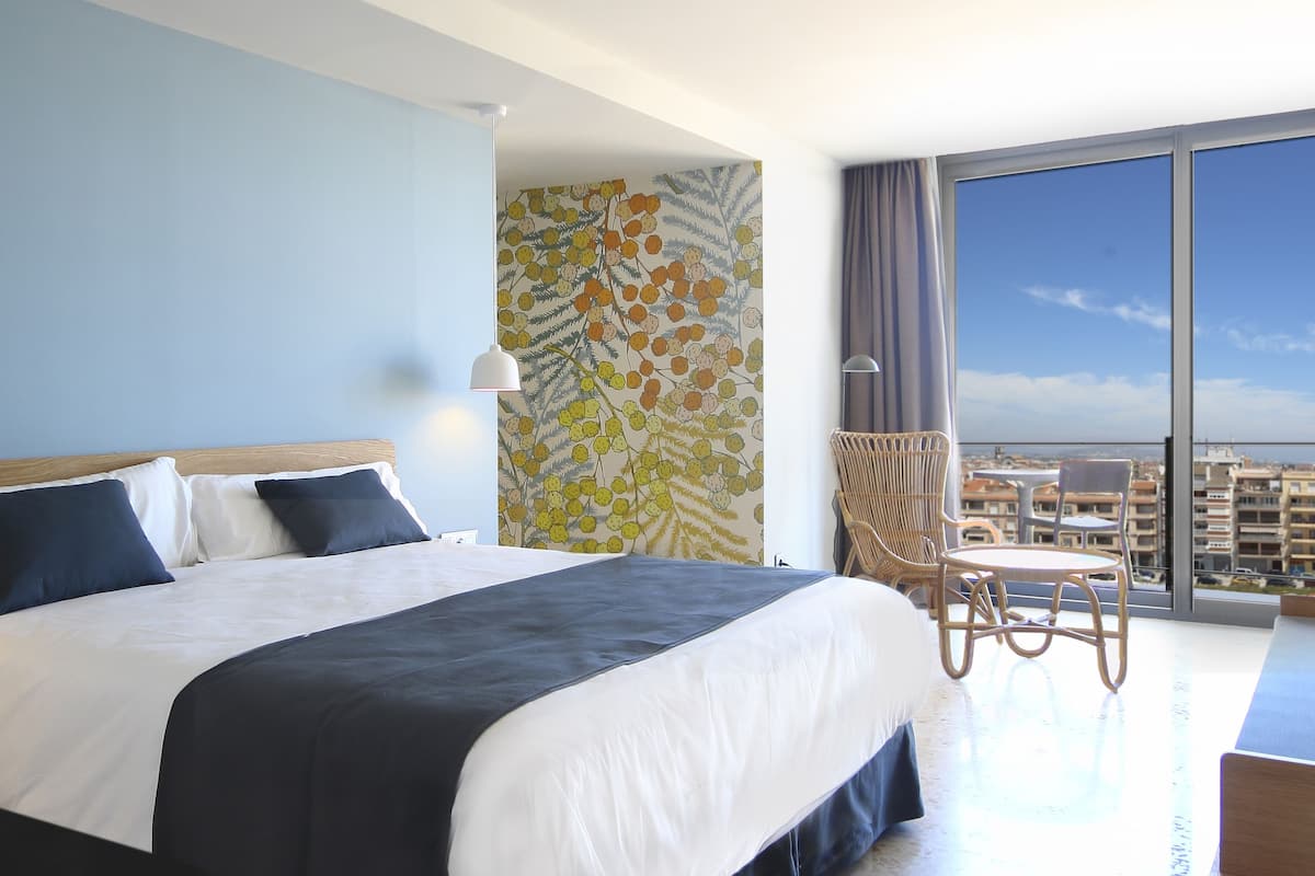 Ein Hotelzimmer mit einem großen Bett, einem Balkon mit Stadtblick und einem kleinen Tisch mit Stühlen.