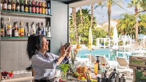 A bar area with a view of a pool, bar shelves stocked with bottles, and a grill.