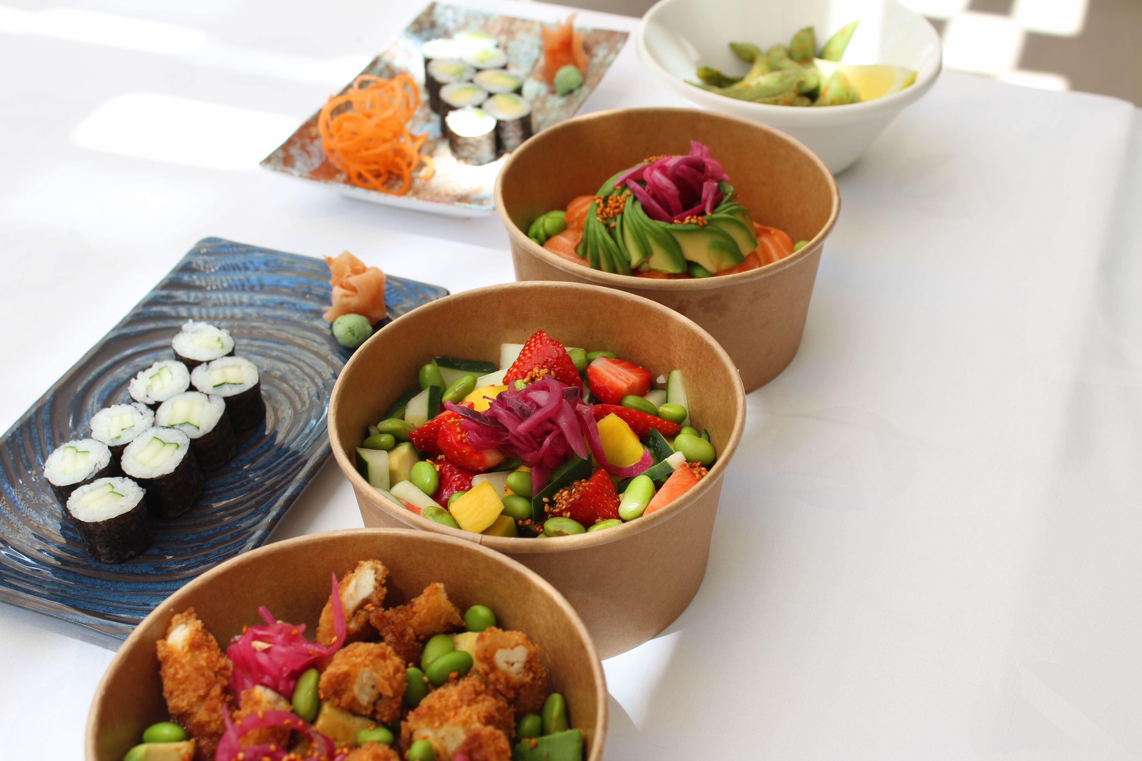 Een tafel met diverse soorten eten, waaronder sushi, salades en een gerecht met groene groenten en rode uien.