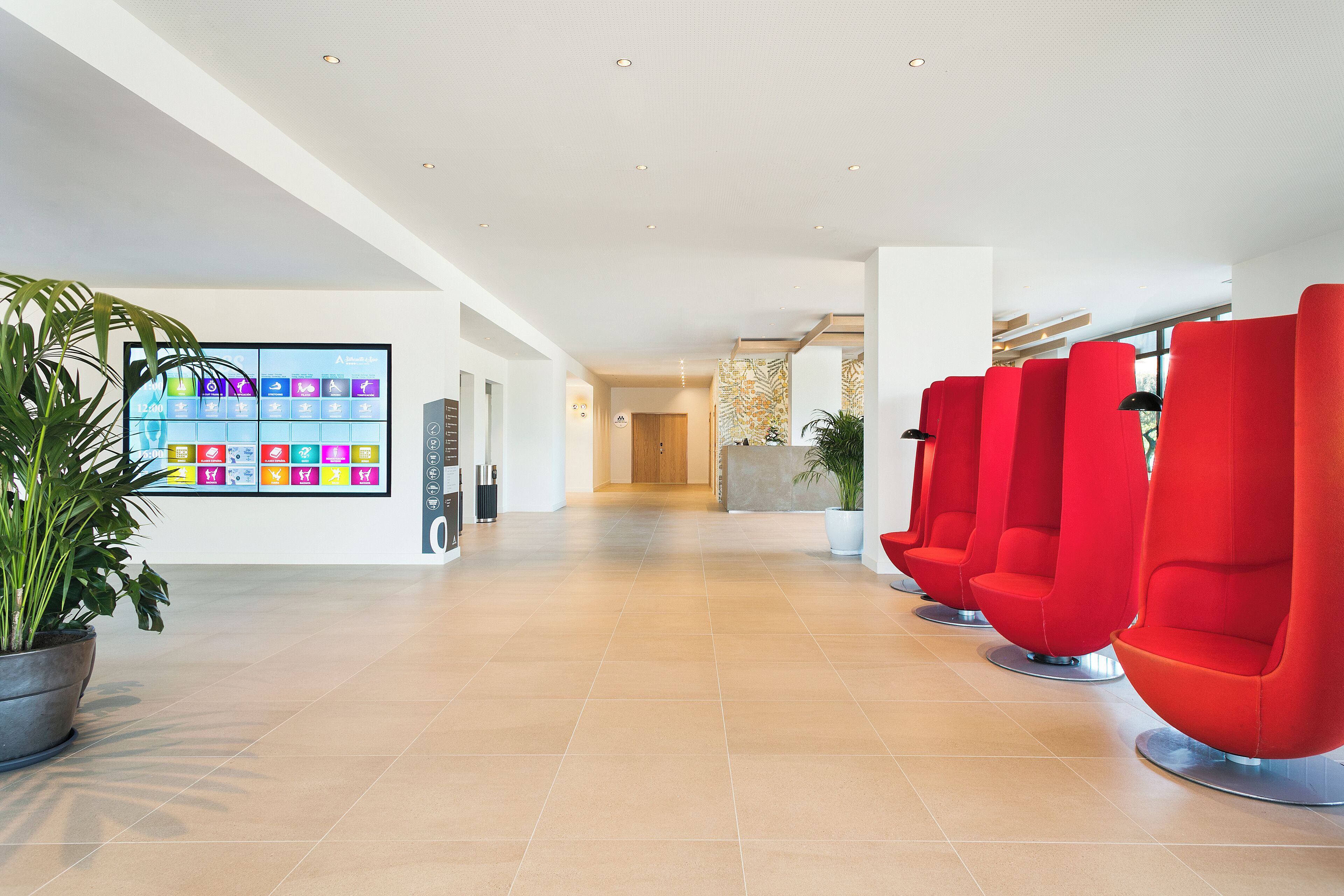 A spacious lobby with a tiled floor, a reception desk, and red seating areas.