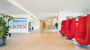 A spacious lobby with a tiled floor, a reception desk, and red seating areas.