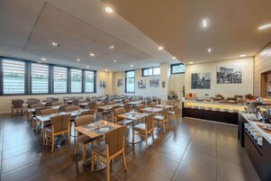 Un'ampia sala da pranzo con diversi tavoli e sedie, ampie finestre e un buffet con una varietà di pietanze.