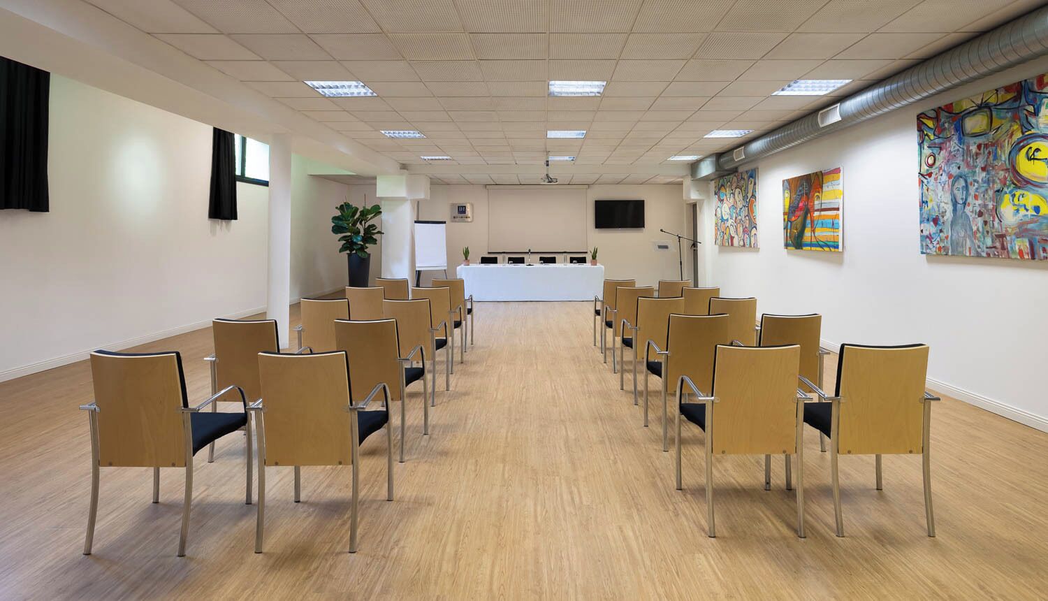 Une salle de conférence avec des rangées de chaises, un écran de projection et un tableau blanc.