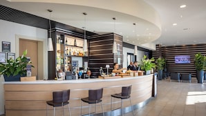 A modern bar area with a curved counter, bar stools, and a television screen mounted on the wall. - iH Hotels Milano Gioia (Milan)
