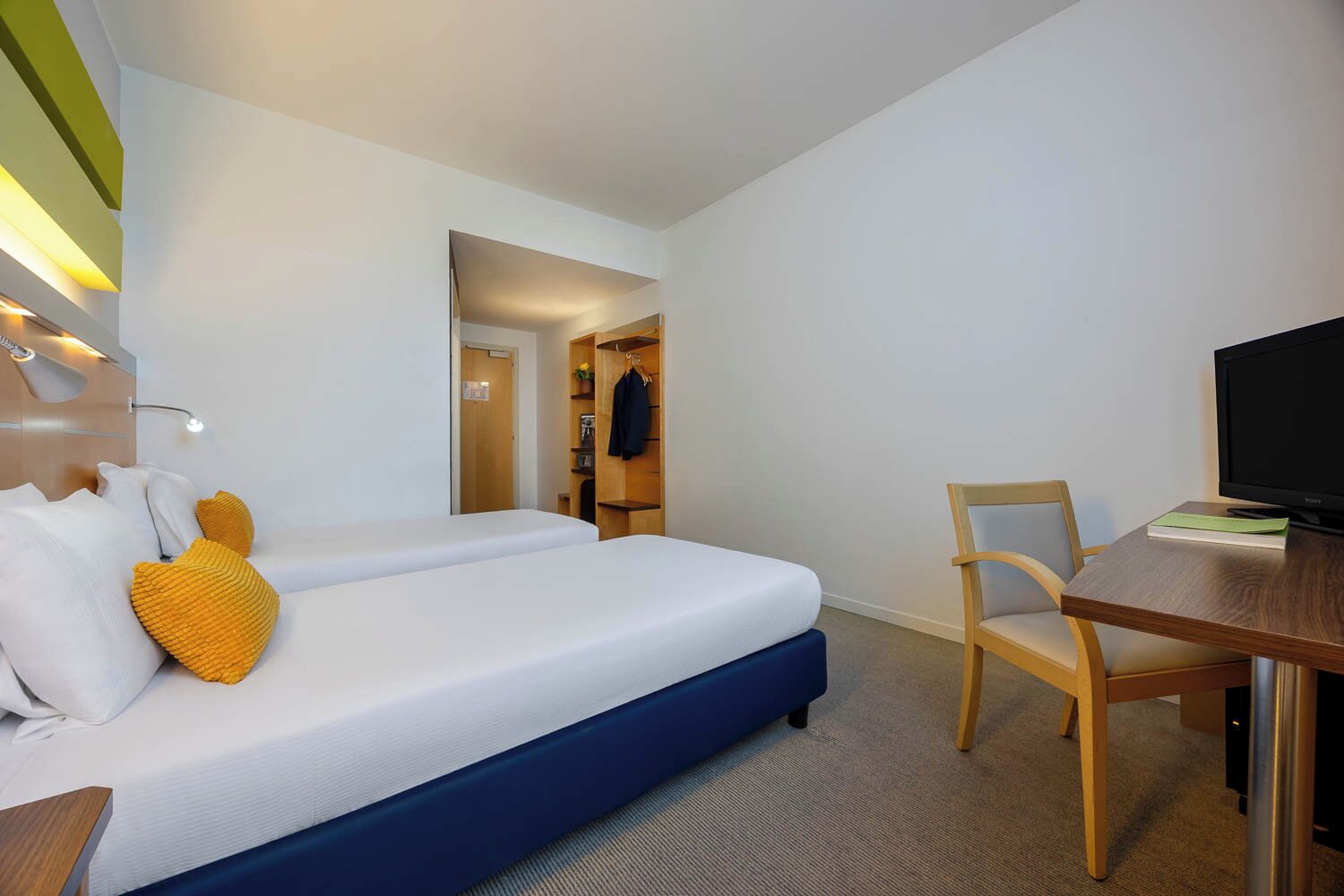 Una habitación de hotel con cama, escritorio, silla, televisor y armario.