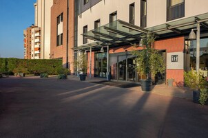 Ingresso di un hotel con portico, vetrate e piante in vaso.