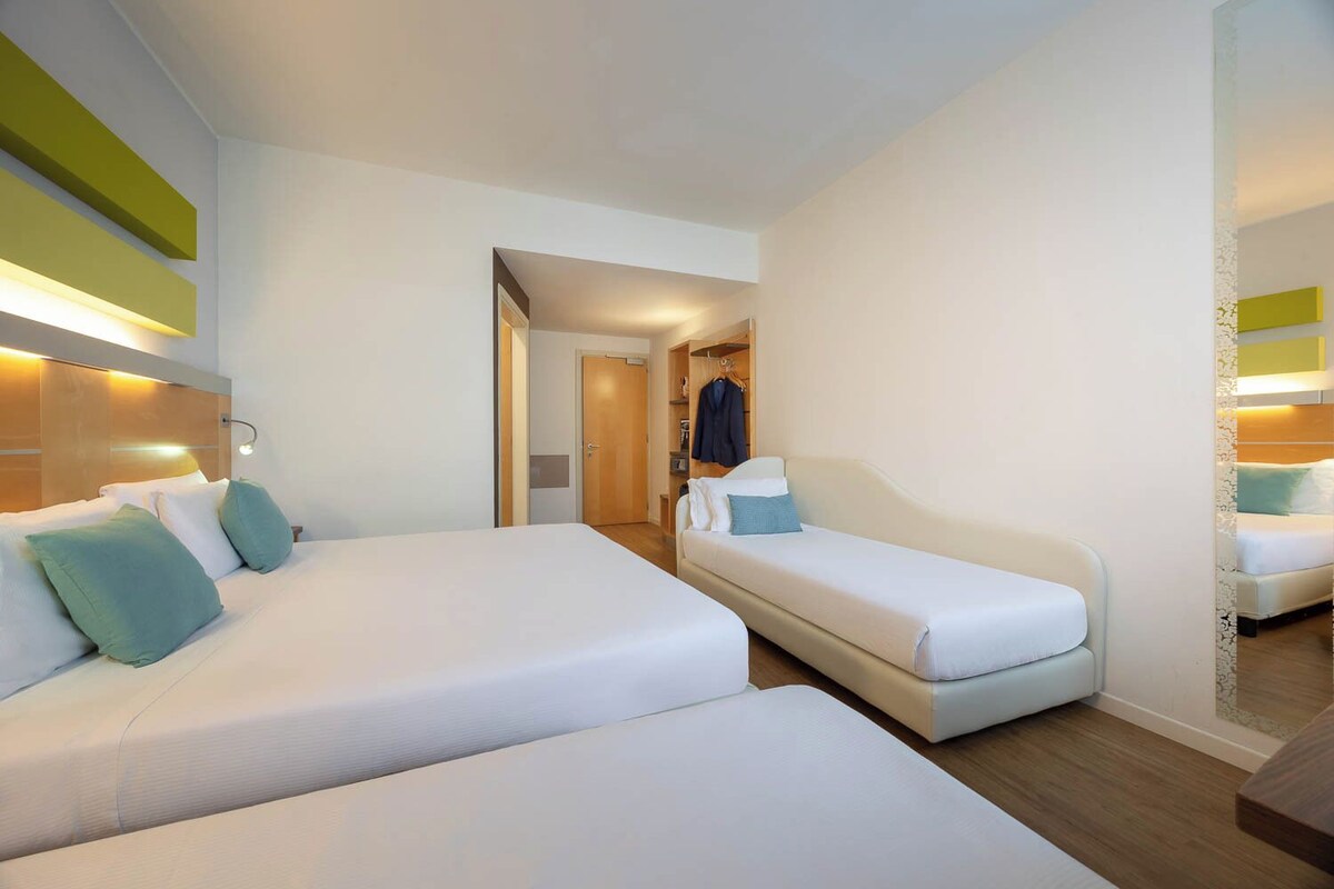 Habitación de hotel con dos camas, cabecera de madera, vestidor y un espejo.