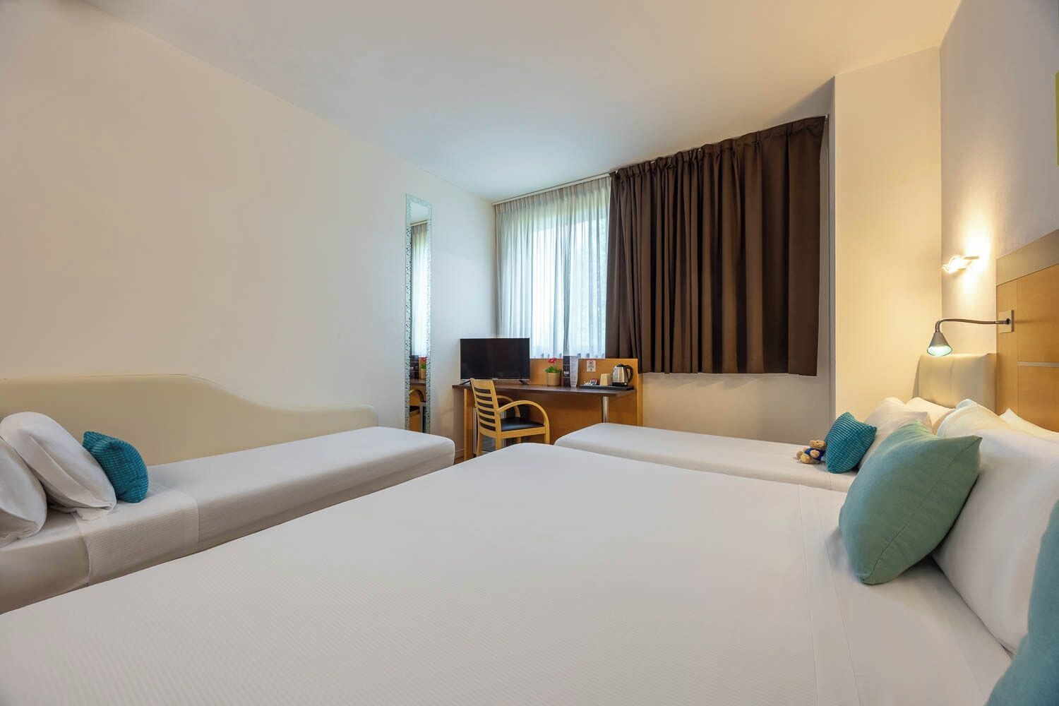 A hotel room with two single beds, a desk, a chair, a television, and a window with curtains.