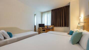 A hotel room with two single beds, a desk, a chair, a television, and a window with curtains.