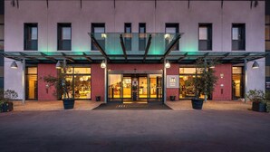 A hotel entrance with a glass canopy, red brick facade, and potted plants. - iH Hotels Milano Gioia (Milan)