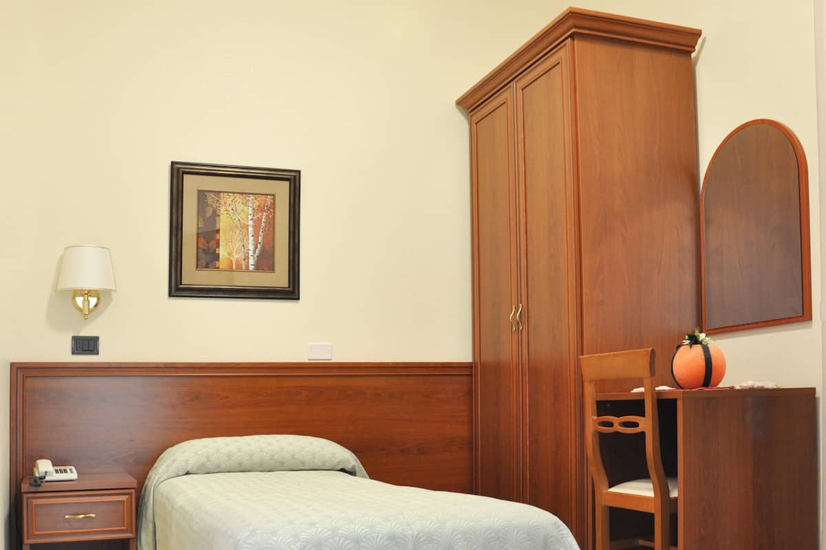 Un dormitorio ordenado con cama, mesita de noche, lámpara, cuadro enmarco, armario, silla y una pequeña mesa.