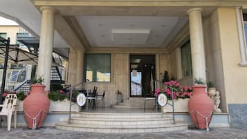 A hotel entrance with a covered porch, steps leading to the door, and large potted plants.