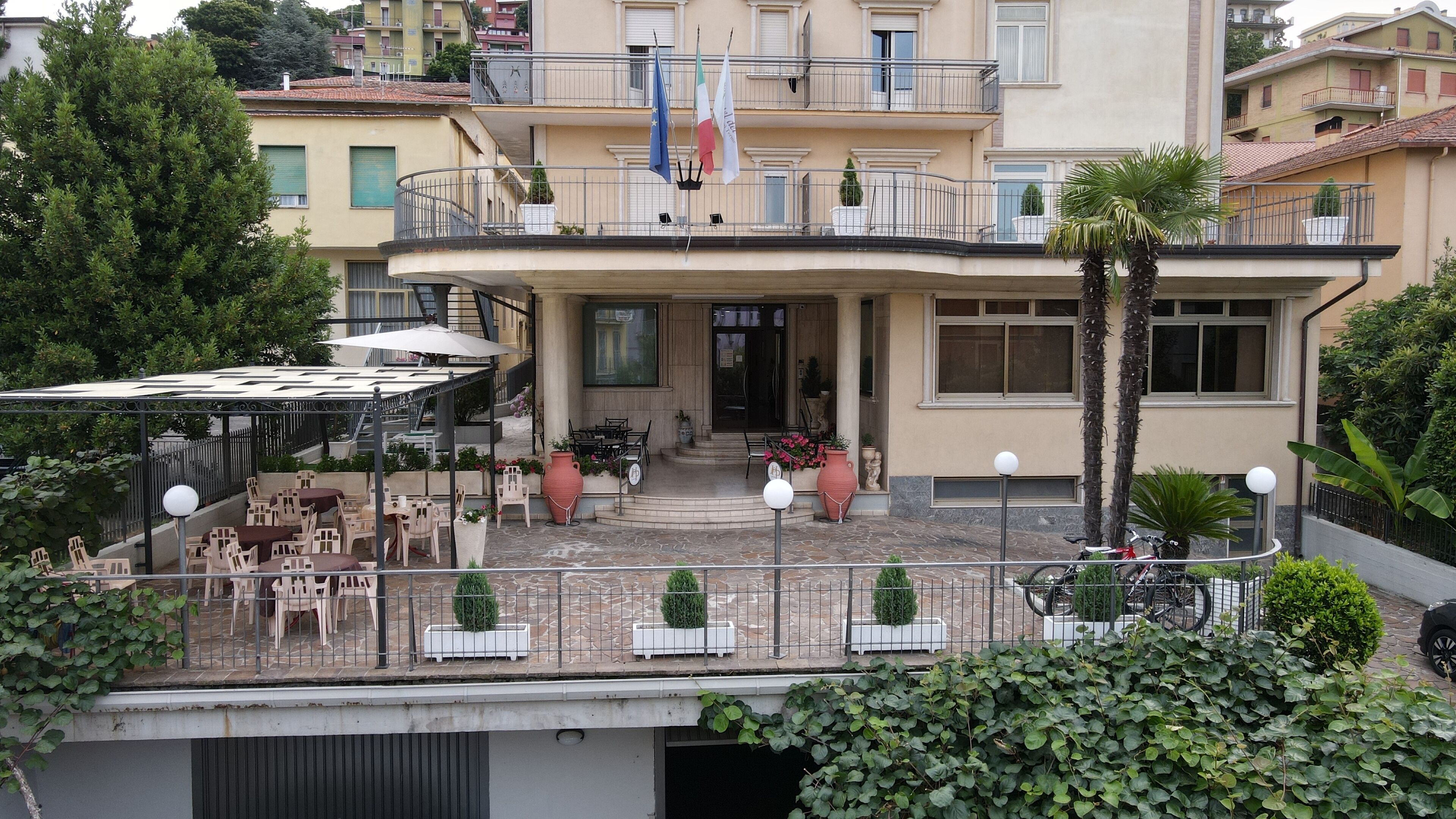A hotel with a covered outdoor seating area, multiple balconies, and potted plants.