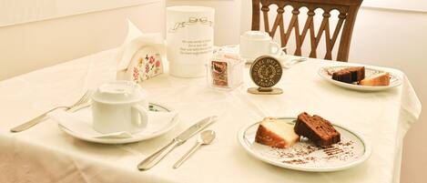 A table set for a meal with a white tablecloth, a plate of cake, a cup, a teapot, and a decorative item.