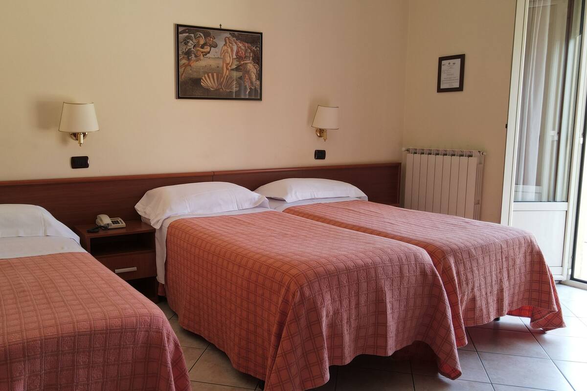 Habitación de hotel con dos camas individuales, una mesita de noche con teléfono, un cuadro en la pared y una ventana con cortinas.
