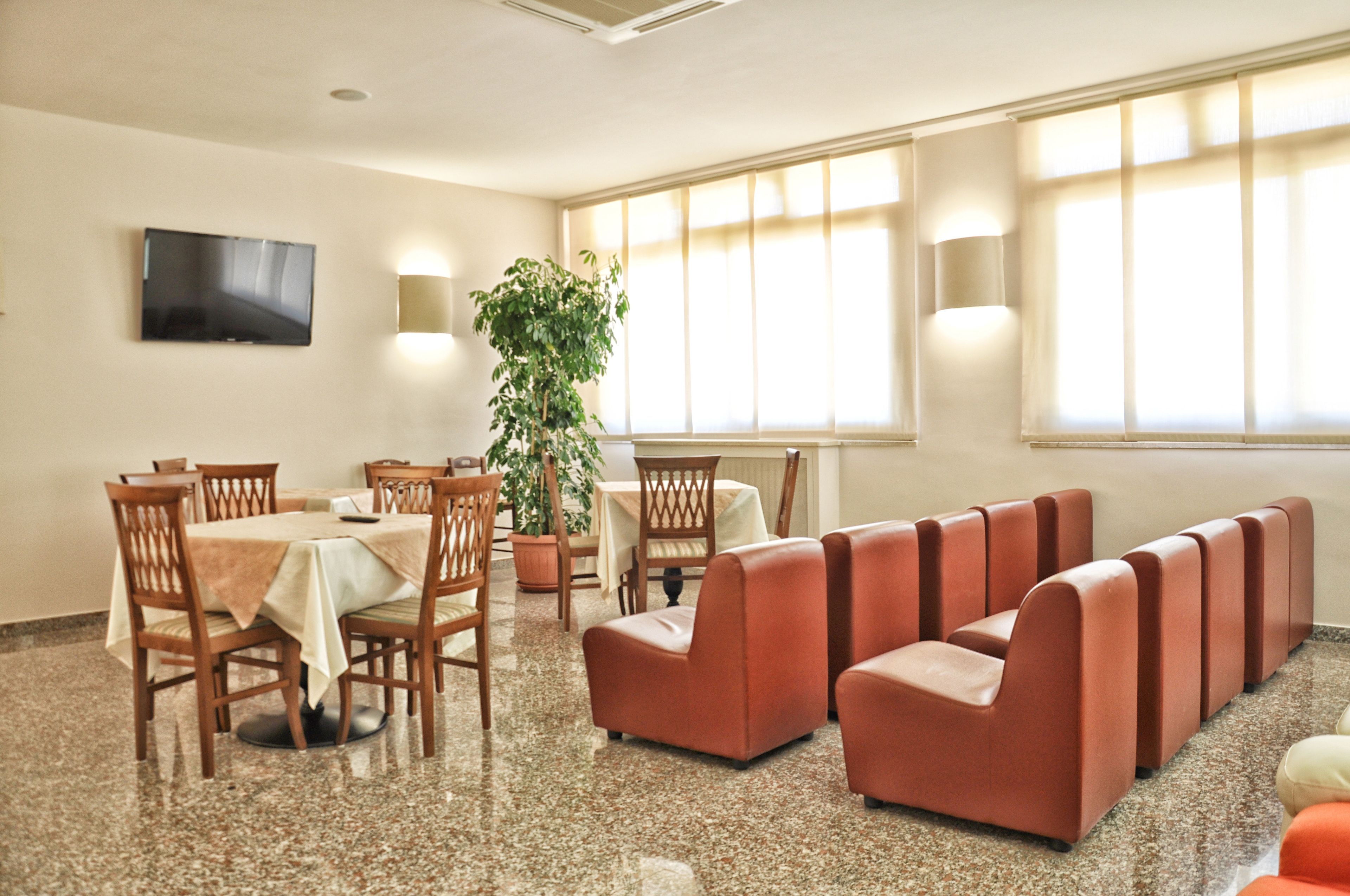 A dining area with a table set for four, surrounded by wooden chairs, a sofa, and a potted plant.