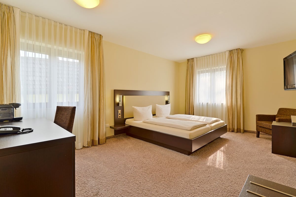 A hotel room with a bed, a desk, a chair, and a television.