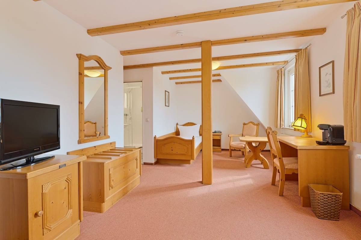 A room with a bed, a desk, a chair, a television, and a bathroom visible through an open door.