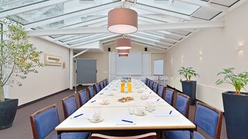 Ein Konferenzraum mit langem Tisch, blauen Stühlen, einer großen Pflanze und einer Glasdecke.