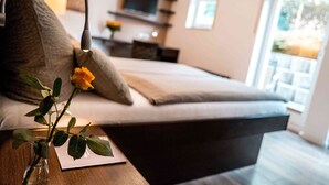A modern bedroom with a bed, a bedside table, a vase with a single rose, and a television in the background. - Hotel-Restaurant Zur Post (Bonn)