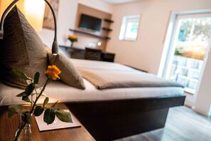 Un dormitorio moderno con una cama, una mesita de noche, un jarrón con una sola rosa y un televisor al fondo.