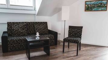 Een kamer met een bank en een stoel, een kleine tafel met een kaars, een lamp en een schilderij aan de muur.