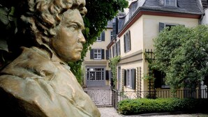 Eine Statue in einem Garten, im Hintergrund ein Gebäude.