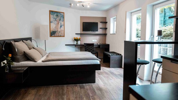 A modern bedroom with a large bed, a desk, a TV, and a window with a view of greenery. - Hotel-Restaurant Zur Post (Bonn)