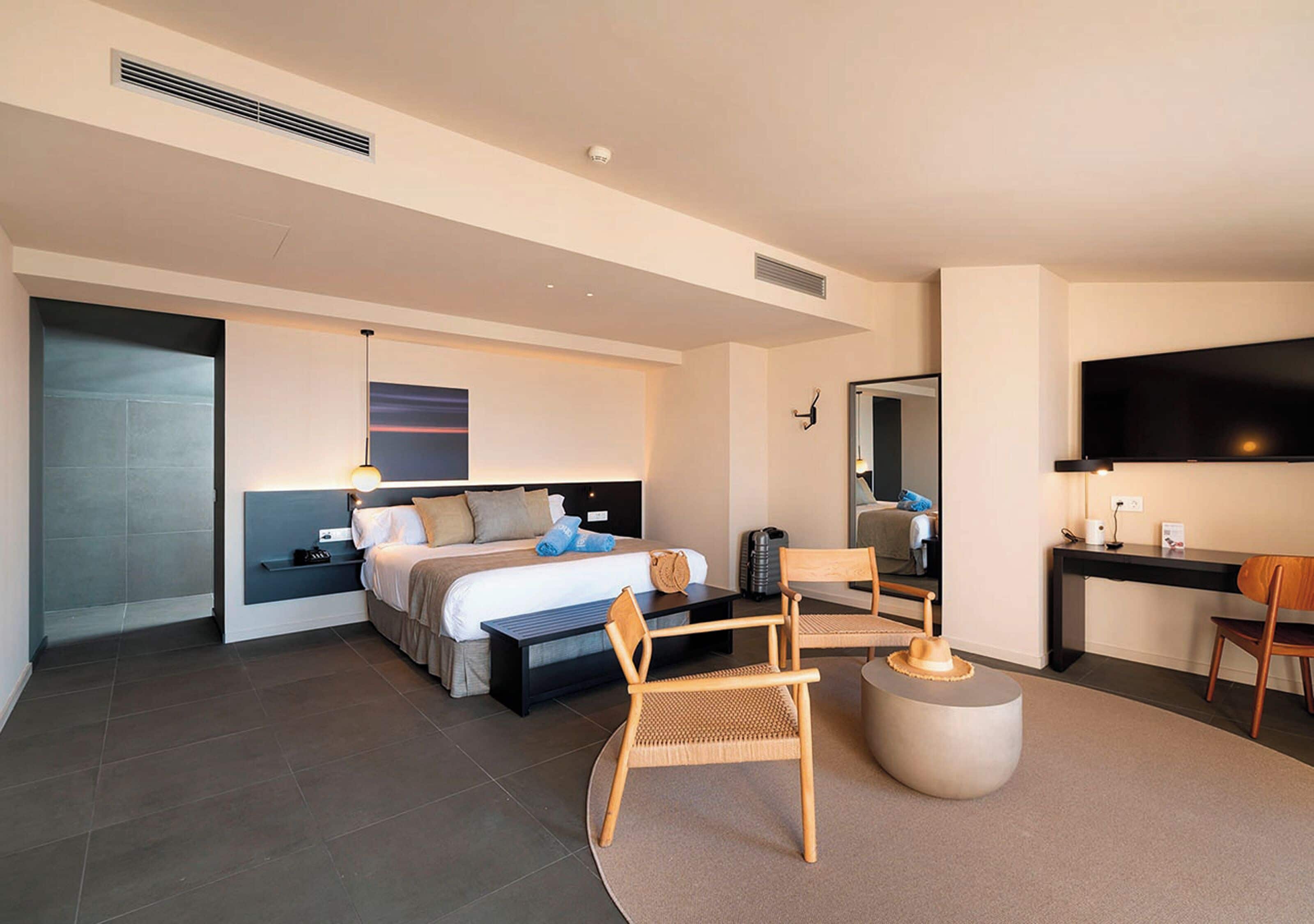 A modern hotel room with a large bed, a desk, a chair, and a TV.
