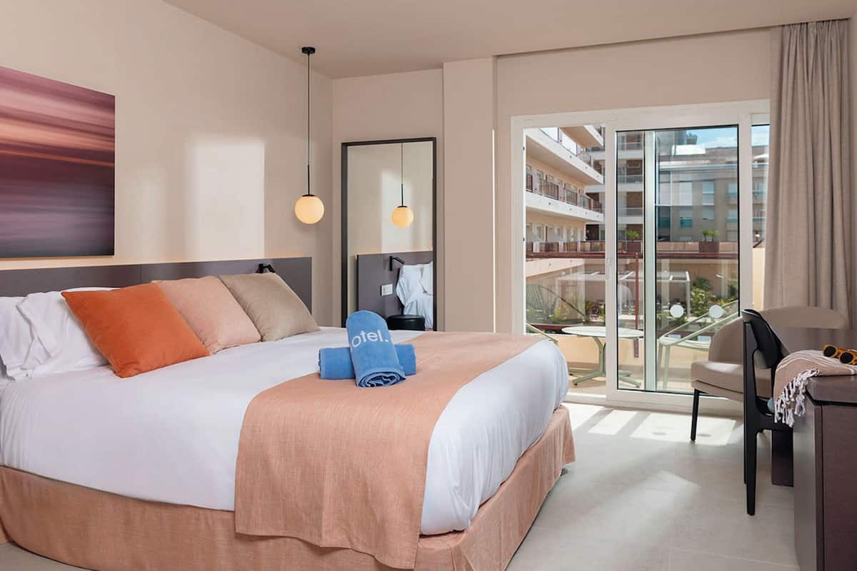 Een hotelkamer met een bed, een bureau, een stoel, een groot raam en uitzicht op het balkon.