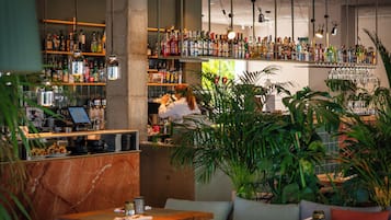 Een bar met flessenkasten vol drank, een bargedeelte en zitplaatsen met potplanten.