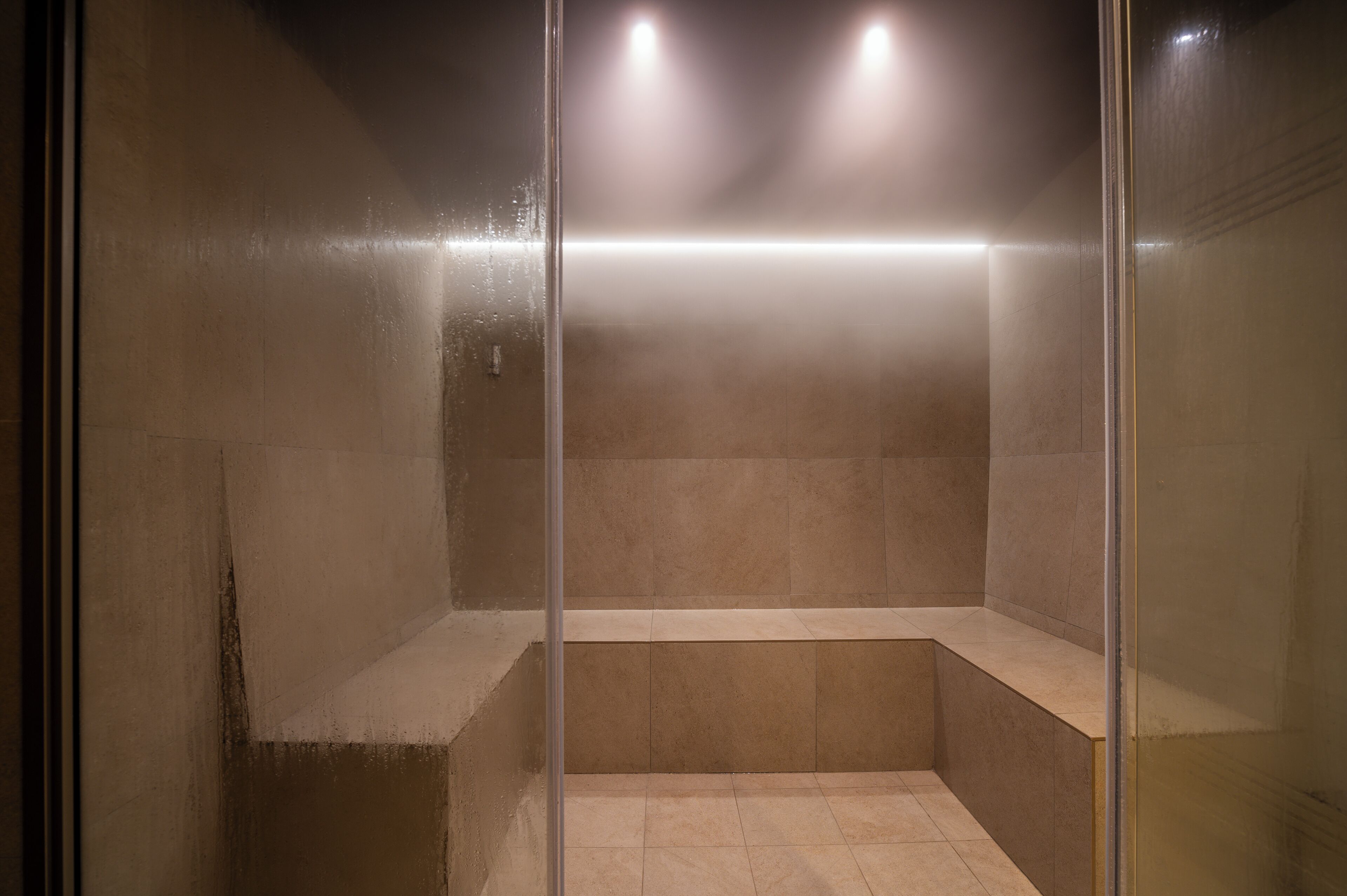 Un box de ducha moderno con puerta de cristal, banco y luces empotradas.