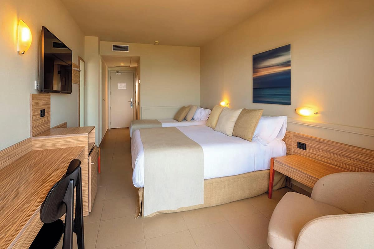 Een hotelkamer met een bed, bureau, stoel en een schilderij aan de muur.