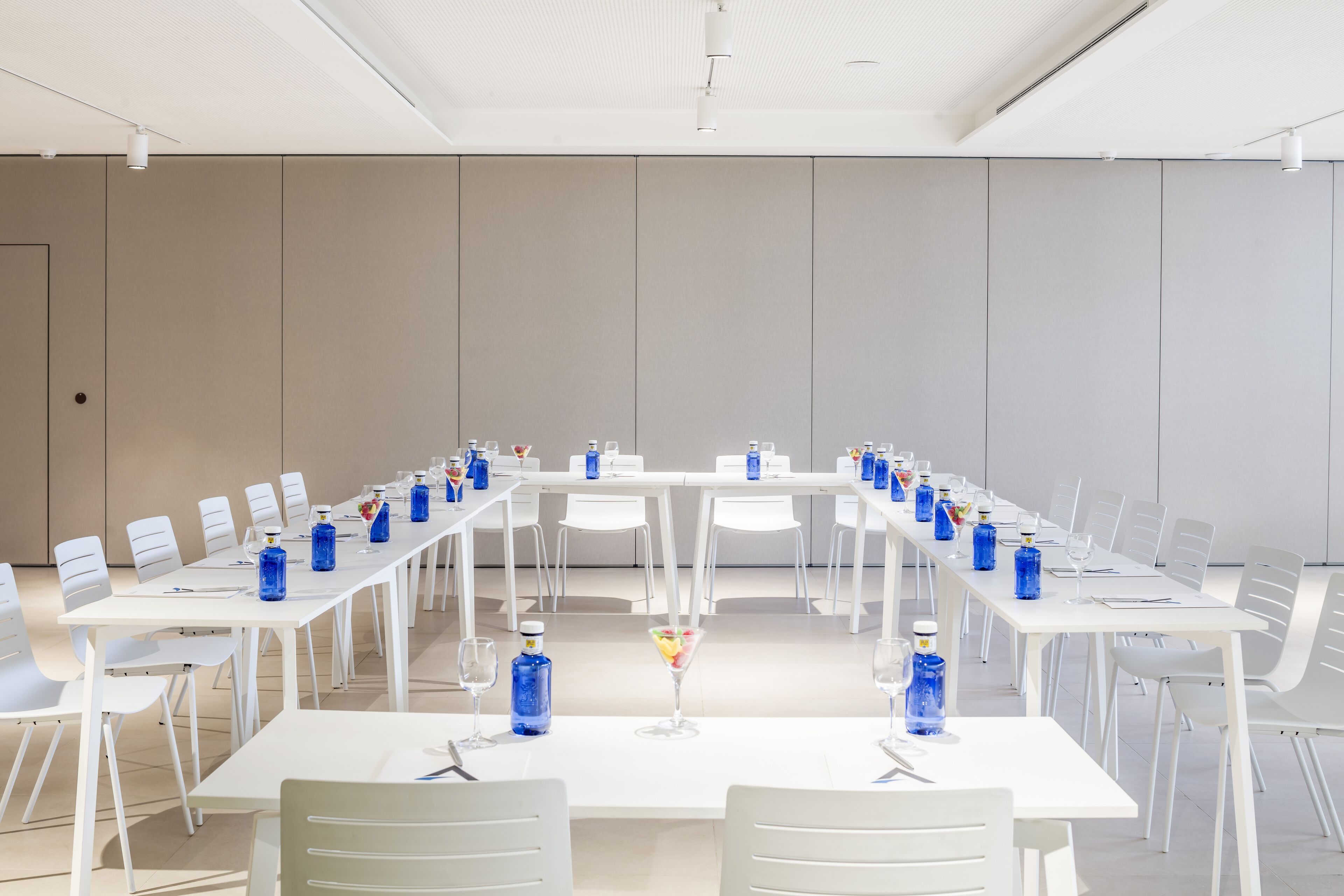 A conference room with white tables and chairs, blue water bottles, and a martini glass.